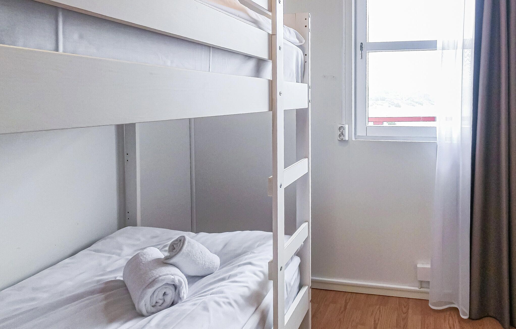 Una cama litera con una toalla enrollada en la cama inferior, una ventana con cortinas y un suelo de madera.