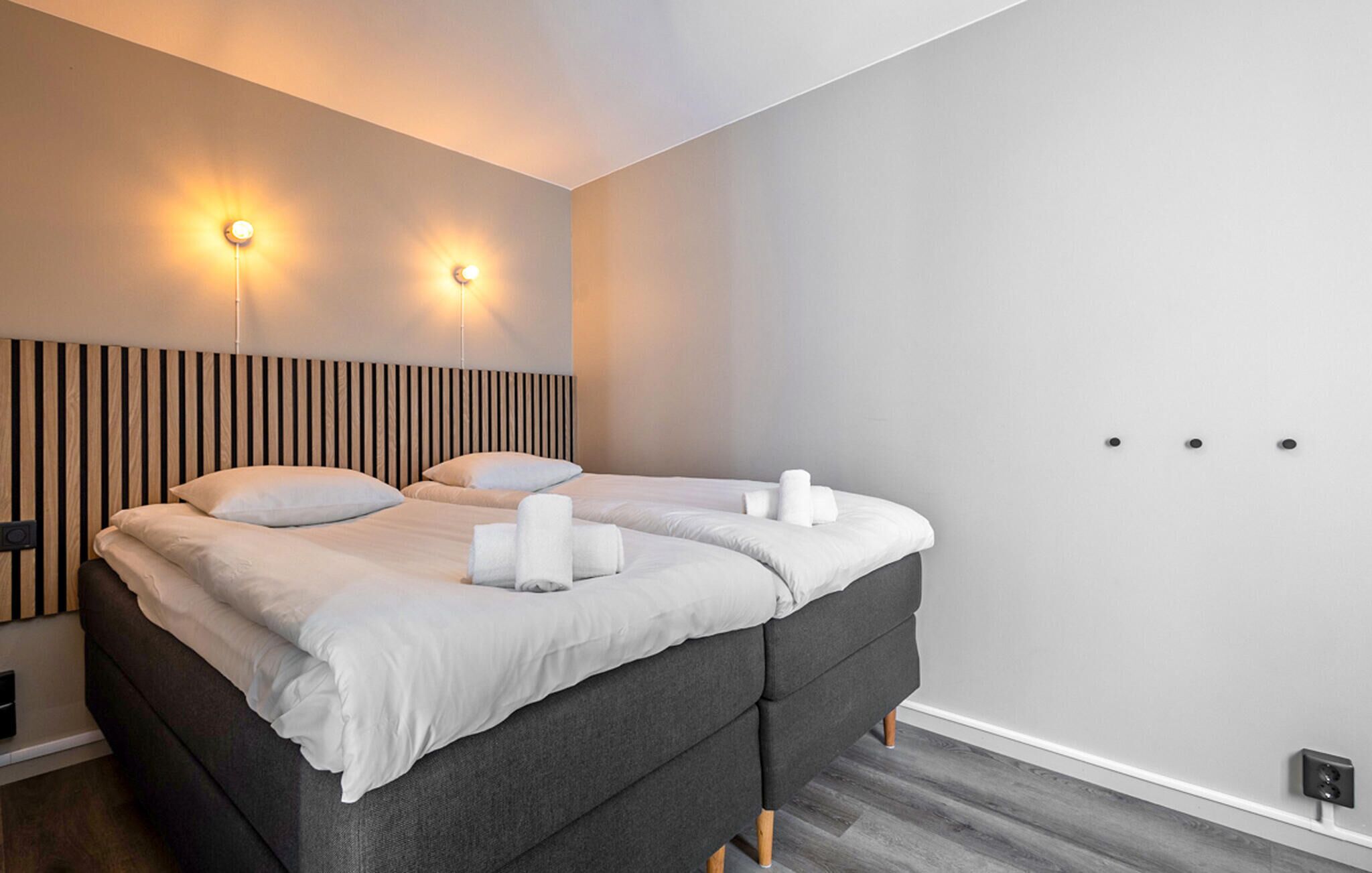 Een moderne slaapkamer met een groot bed, twee wandlampen en een houten hoofdeinde.