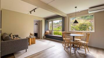 Un salon moderne comprenant un canapé, une table ronde avec des chaises, un banc avec des coussins et de grandes fenêtres donnant sur un paysage verdoyant.