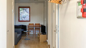 A narrow hallway leading to a living area with a sofa, two chairs, a small table, and a television.