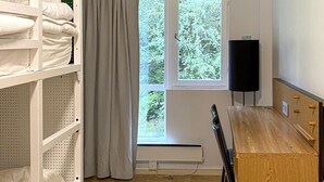 A room with a window, a radiator, a wooden desk, and shelves with folded towels.