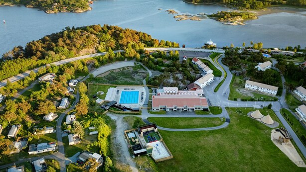 Vista aérea de un complejo turístico costero con piscina, varias edificaciones y una red de carreteras.