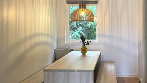Ein Essbereich mit einem Holztisch, Bänken, einer gelben Vase mit Blumen und einer hängenden Leuchte.