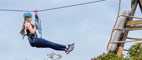 A person zip-lining with safety gear, ropes, and a wooden structure in the background.