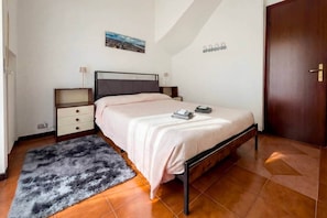 Un dormitorio con cama, mesita de noche, cómoda, alfombra mullida, un cuadro en la pared y una puerta de madera.