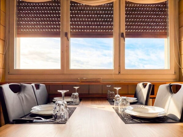 Un comedor con una mesa larga dispuesta para seis comensales, ventanas amplias con vistas y un techo de madera con diseño de celosía.