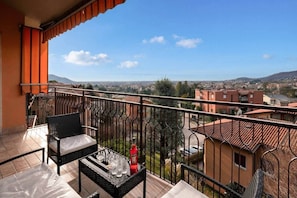 Un balcón con vista a un paisaje urbano, una mesa con vasos y una botella.
