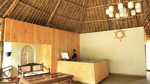A reception area with a wooden desk, a computer, and a clock on the wall. - The Giraffe Cottages Restaurant and Bar (Nairobi)
