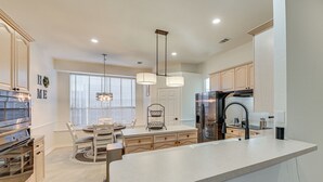 Una cocina moderna con una isla central, electrodomésticos integrados y un comedor con lámpara de araña.