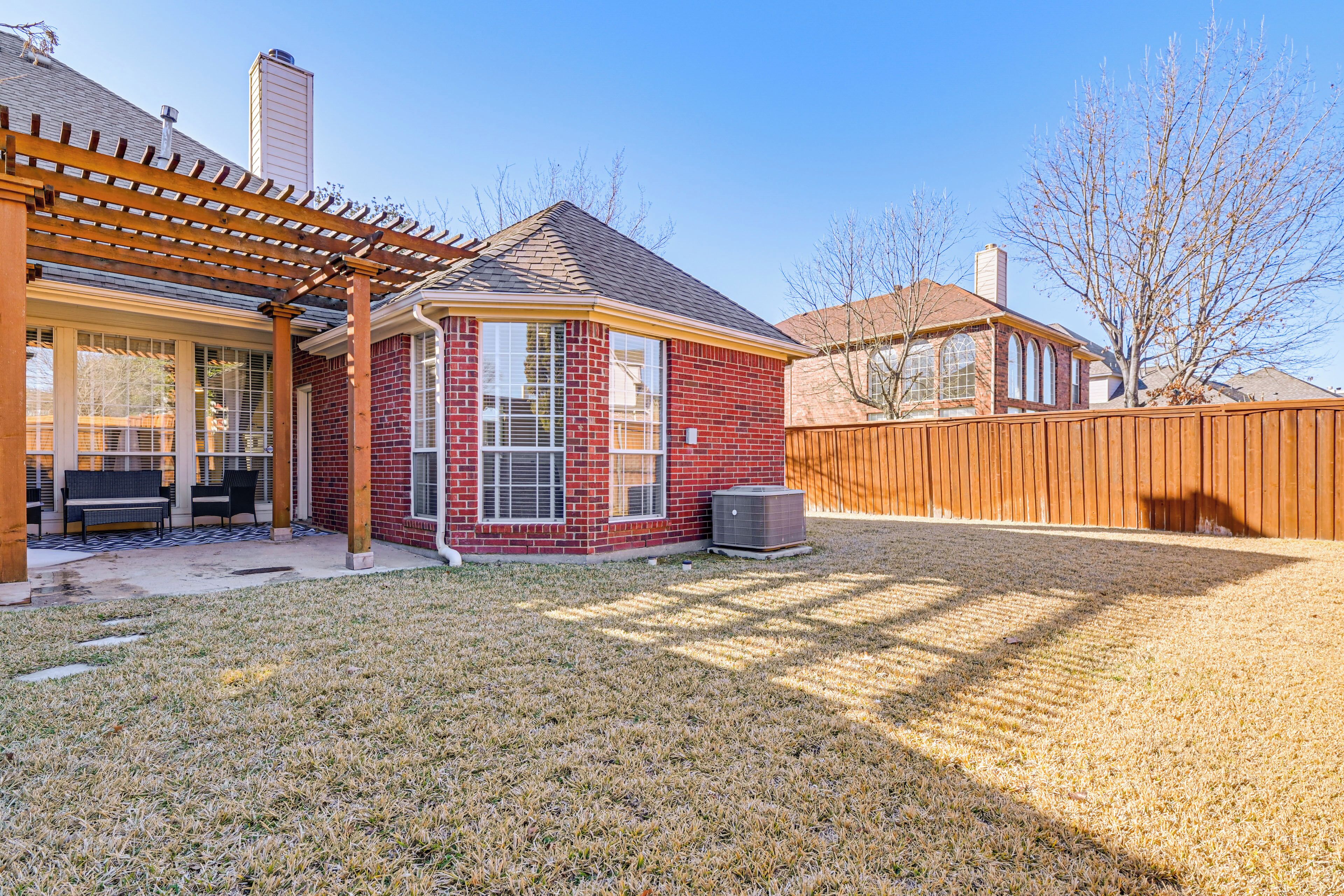 A residential backyard with a covered patio, a brick house, a wooden fence, and a lawn.