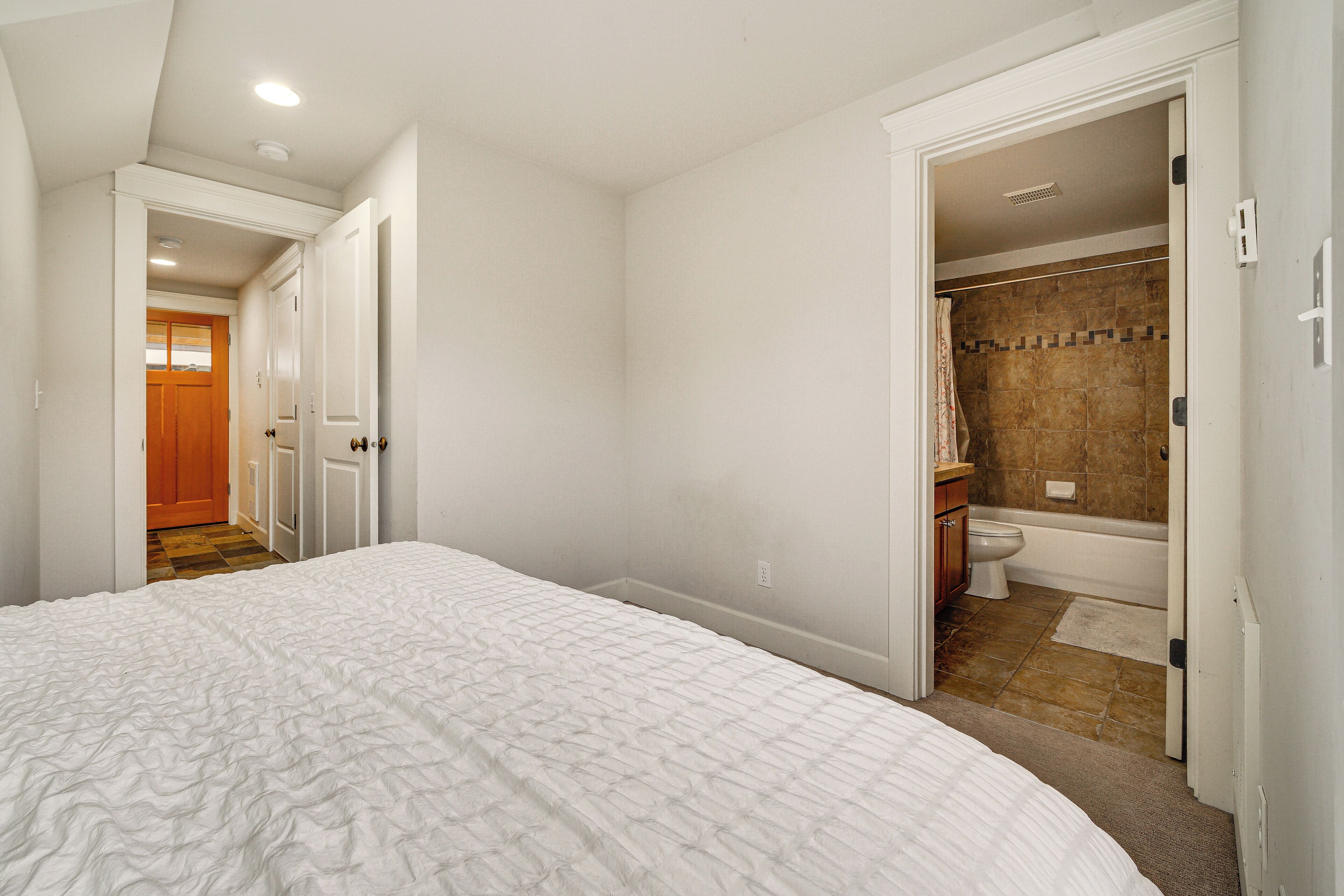 A bedroom with a large bed, a bathroom with a bathtub, and a hallway leading to another room.