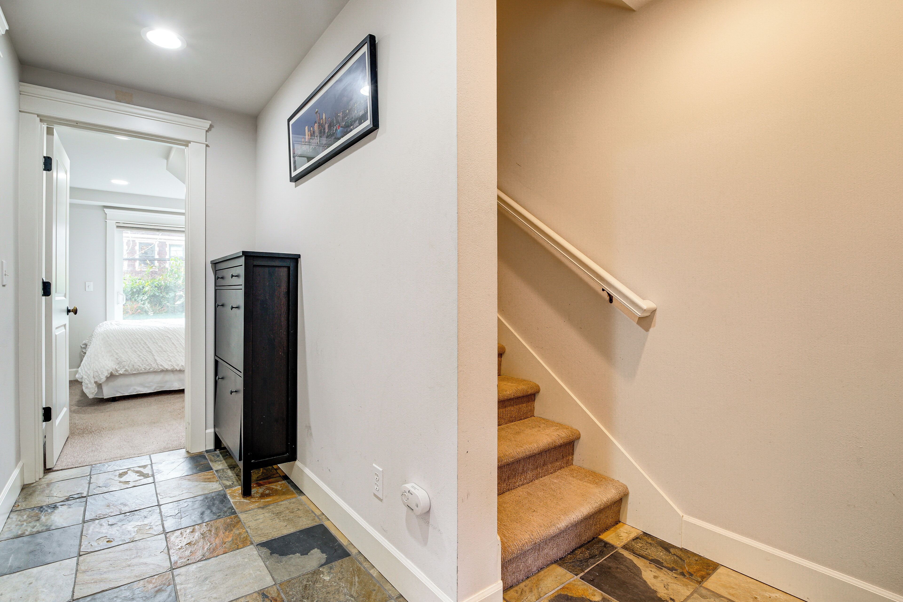 A hallway with a bed, a cabinet, and a staircase.