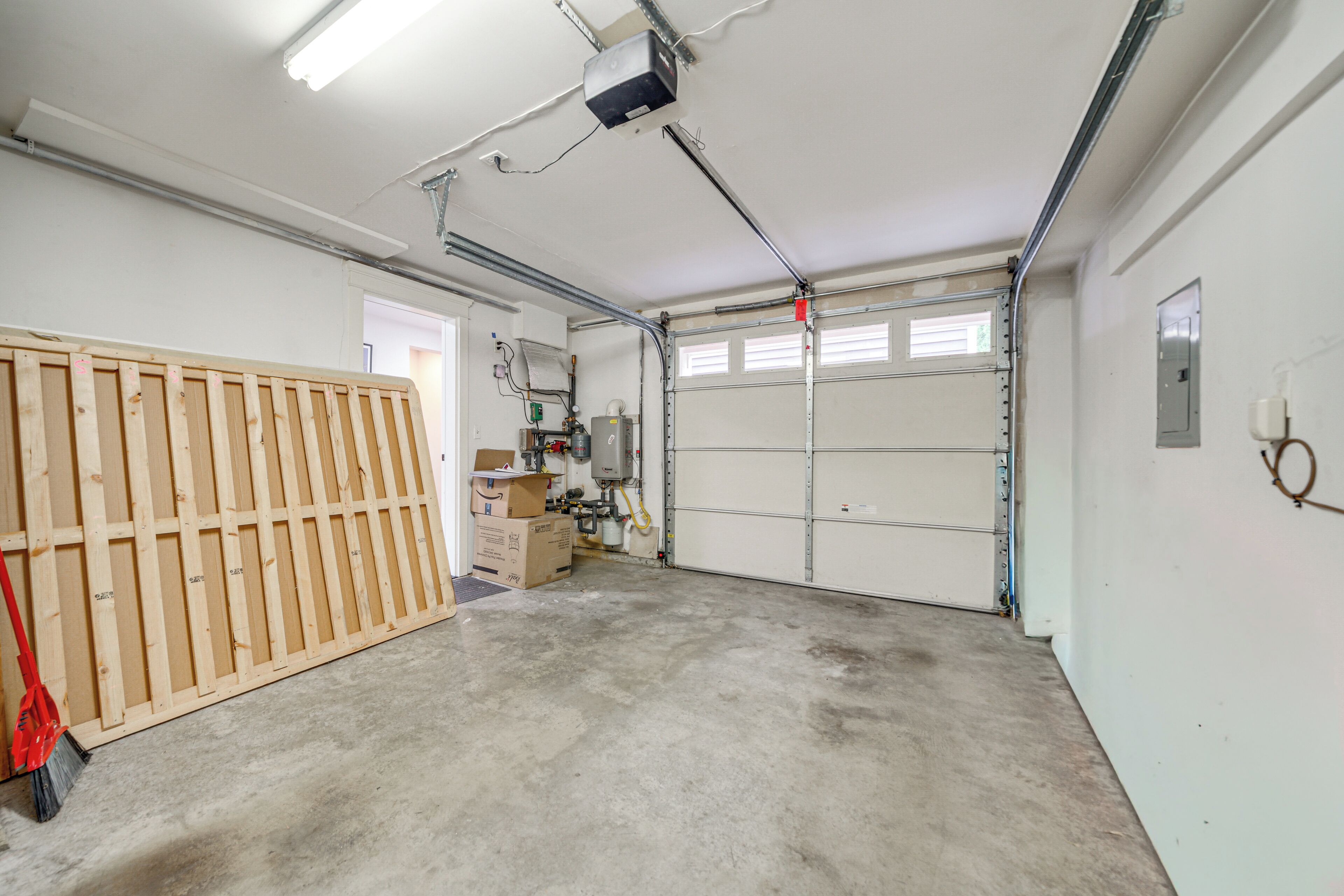 A garage with a wooden fence, a red broom, and a water heater.