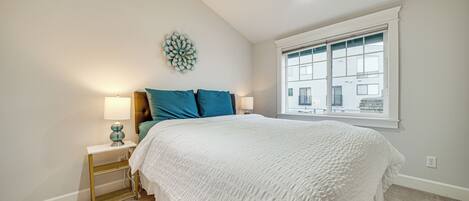 A bedroom with a bed, two bedside tables, a wall clock, and a window.