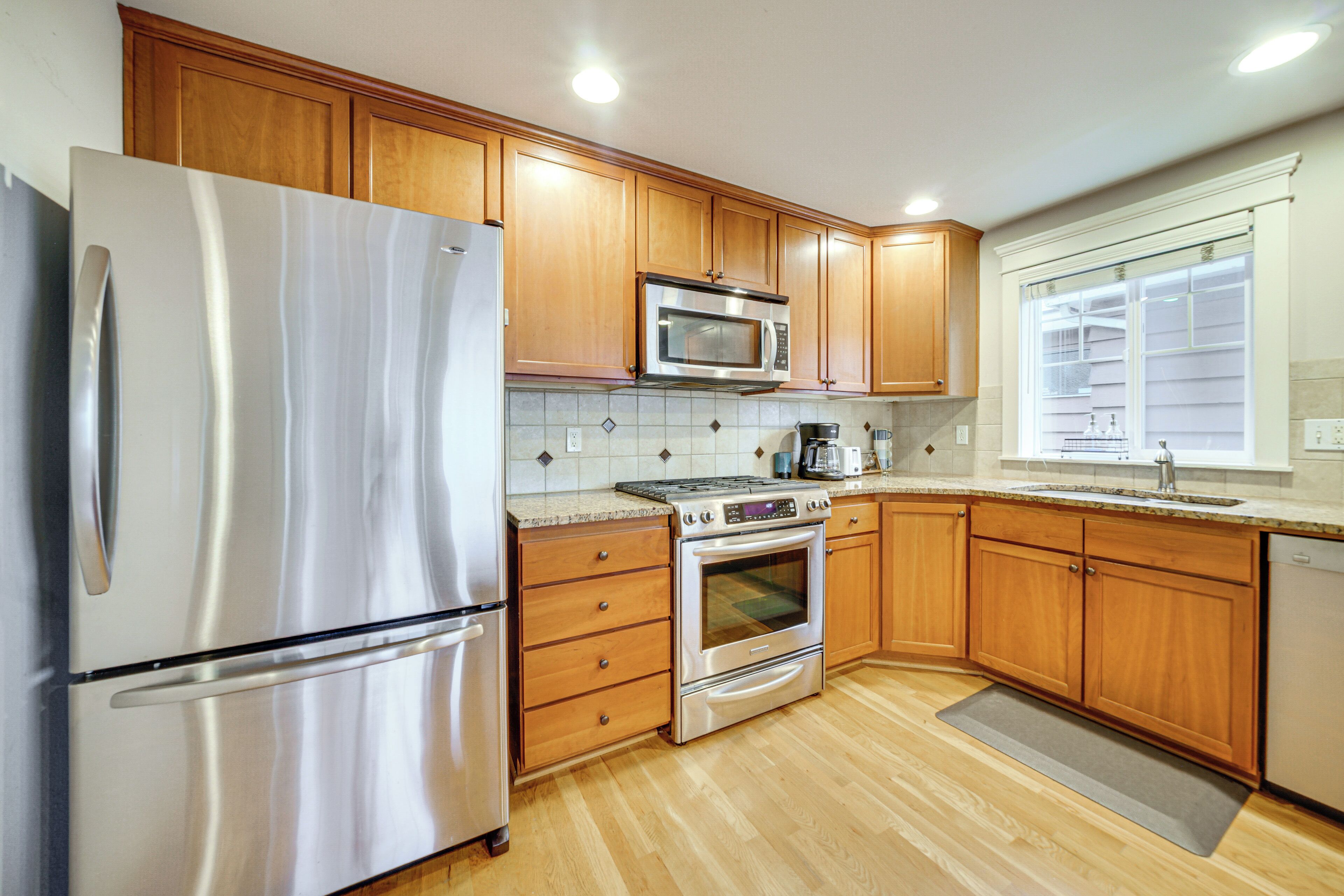 A kitchen with wooden cabinets, stainless steel appliances, and a window with blinds.