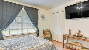 A bedroom with a bed, a TV, a chair, and a table with decorative items. - Shop, Dine & Explore: Home 3 Mi to NRG Stadium (Houston)