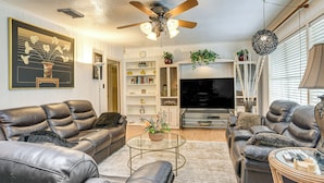 A modern living room with leather sofas, a glass coffee table, and a flat-screen TV. There are shelves with decorative items and a ceiling fan. - Shop, Dine & Explore: Home 3 Mi to NRG Stadium (Houston)