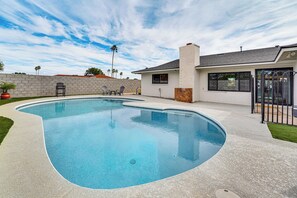 A swimming pool with a curved edge, a brick wall, and a small patio area with chairs.
