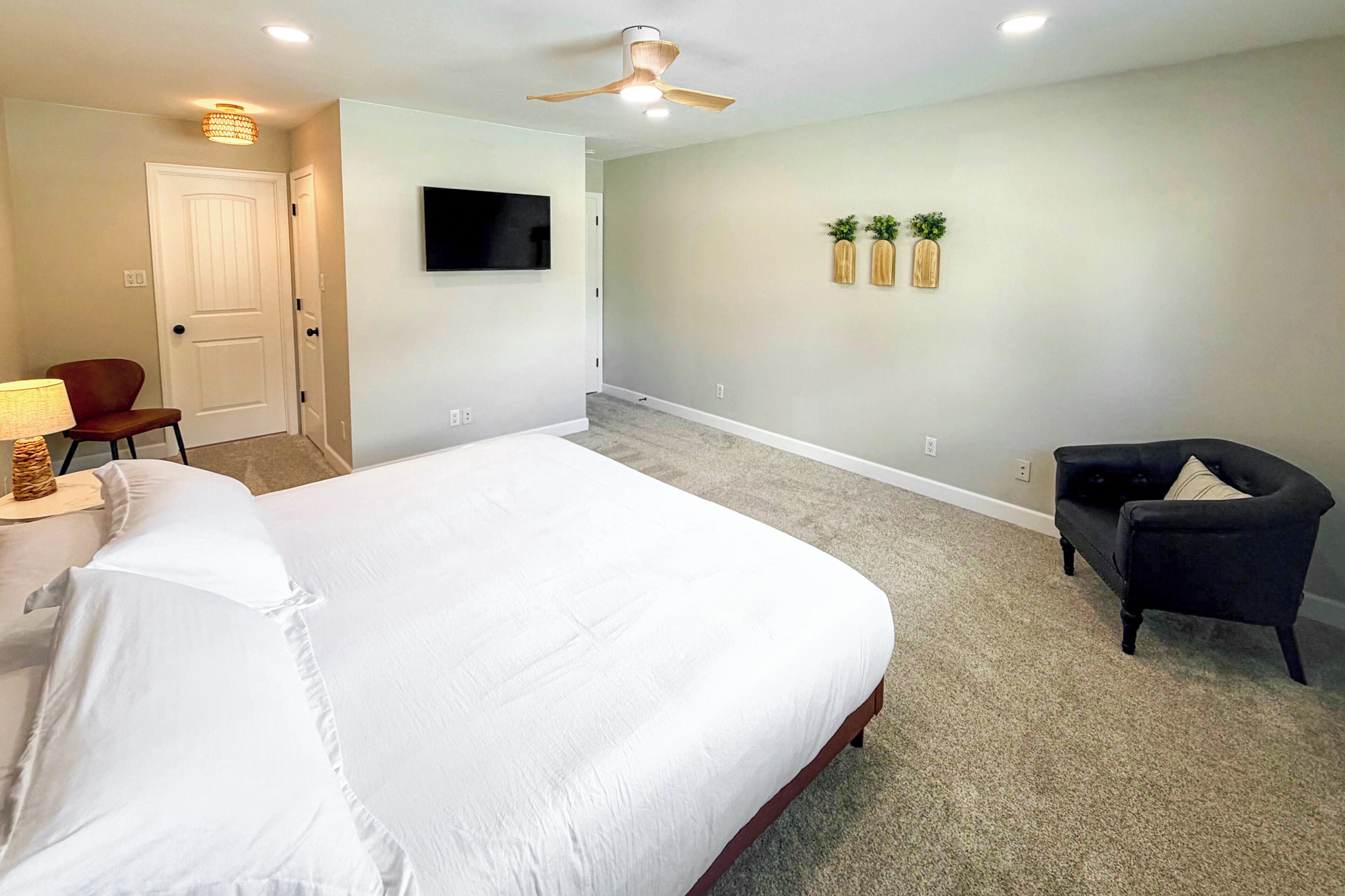 A bedroom with a bed, a chair, a TV, and a door.