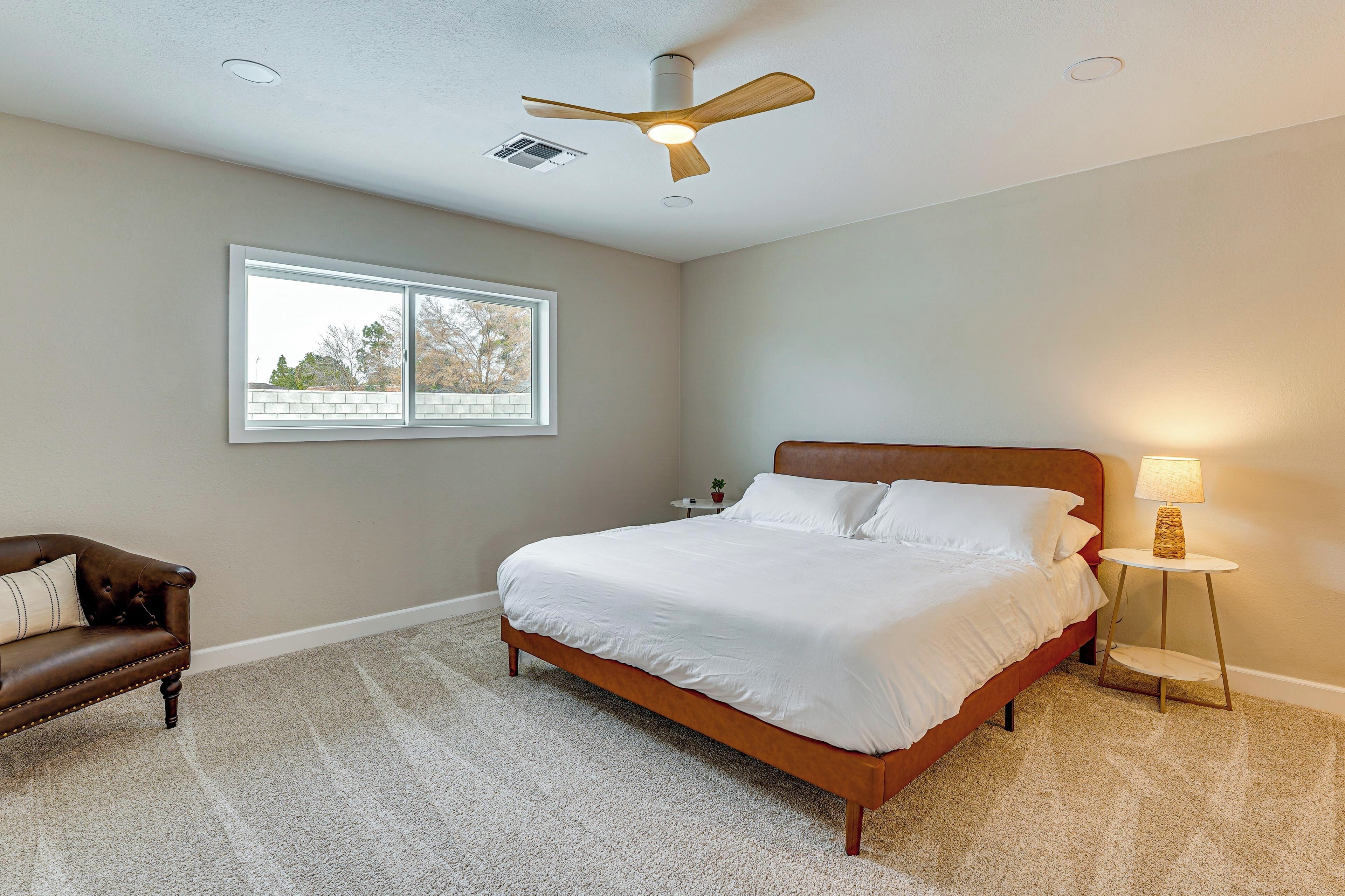 A bedroom with a bed, a ceiling fan, a window, a nightstand, and a lamp.