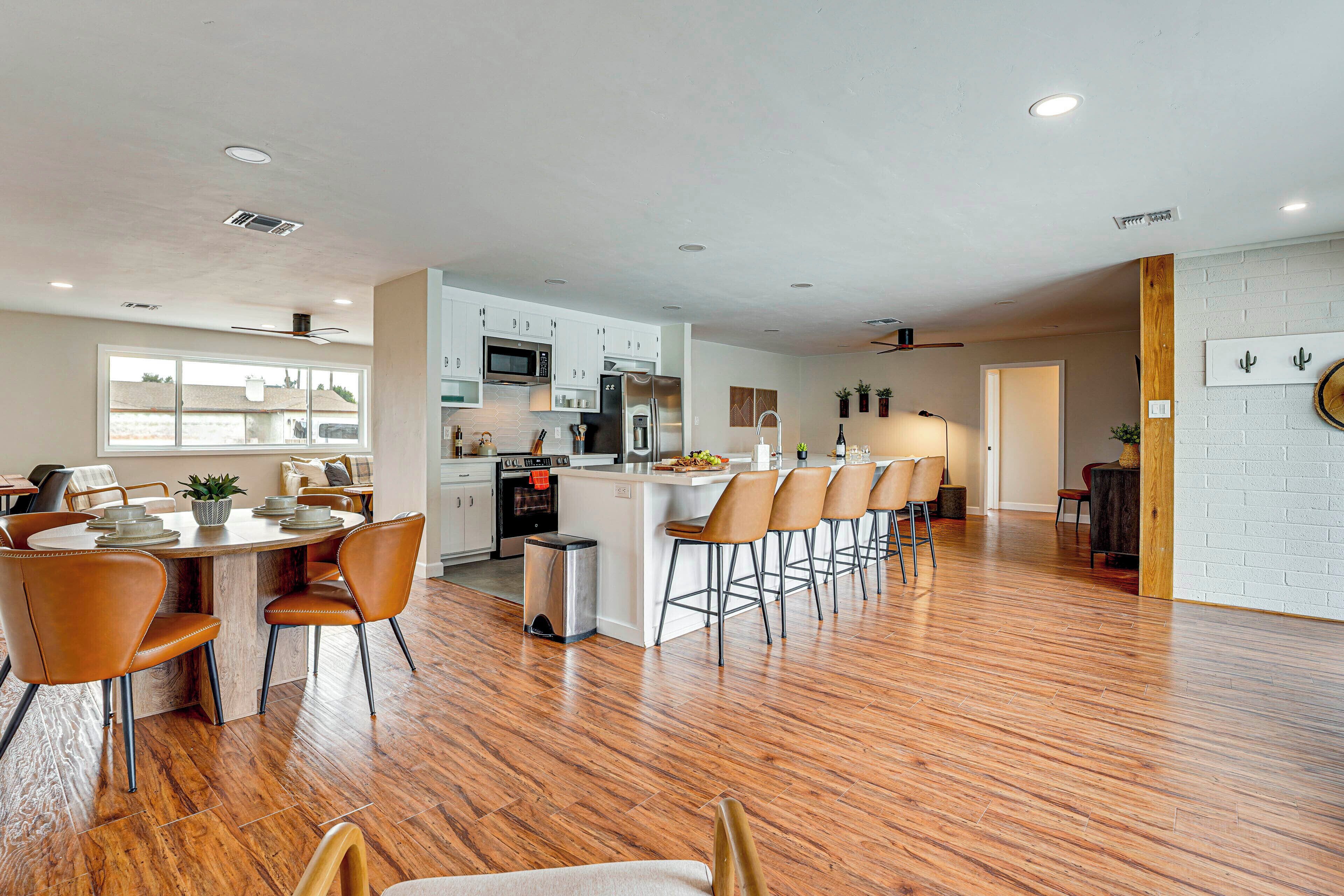 A modern kitchen with white cabinets, a central island with bar stools, and a dining area with a wooden table and chairs.