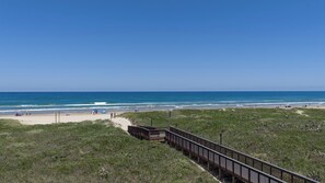 Ein Strand mit einer Holzpromenade, die zum Ufer führt, grasbewachsenen Dünen und dem Meer.