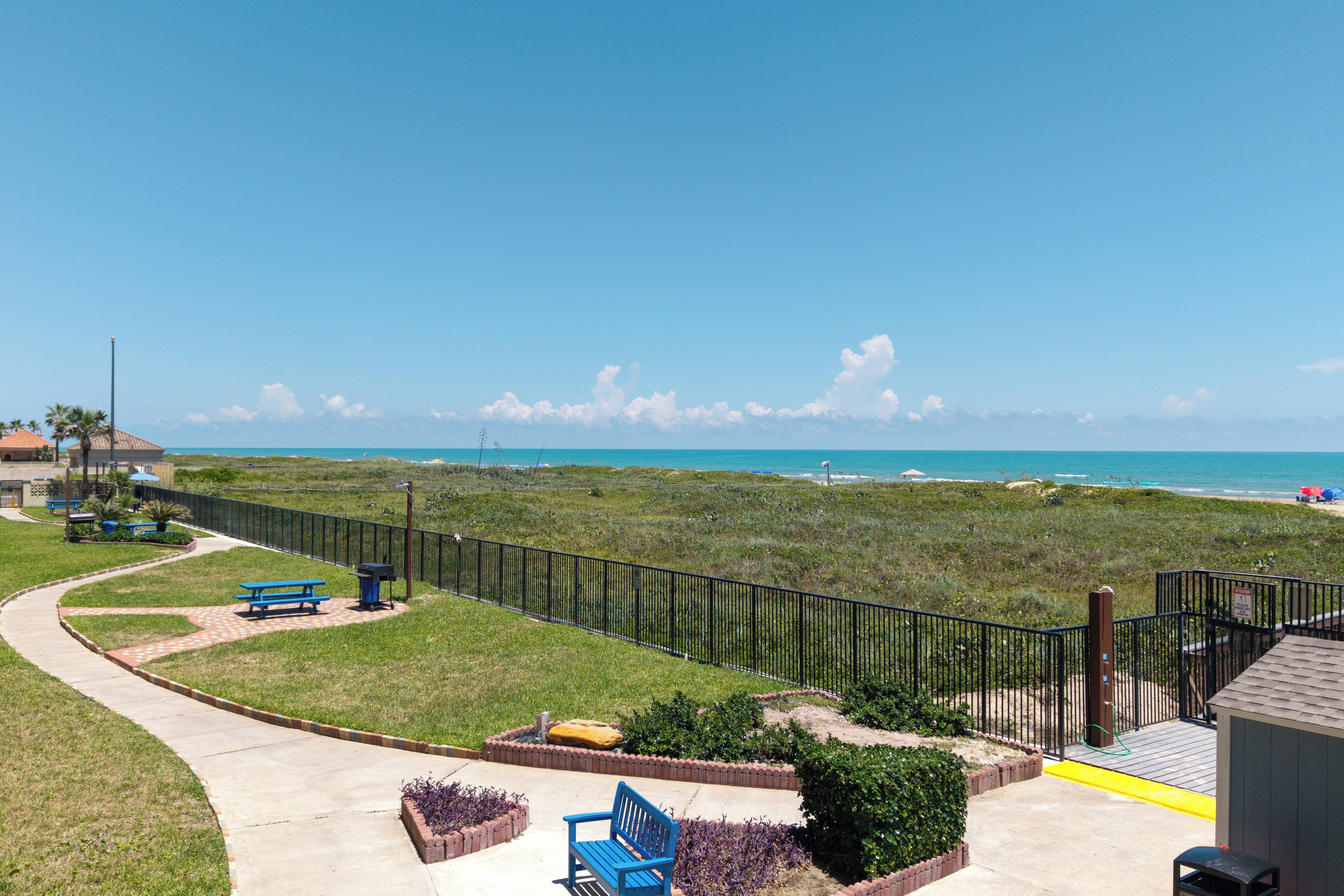 A coastal property with a fenced garden, picnic tables, and a bench.