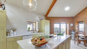 A kitchen with a marble countertop, a wooden bowl with fruits, and a dining area with a table and chairs. - Views of 4 Mtn Peaks! Stunning Scottsdale Oasis (Scottsdale)