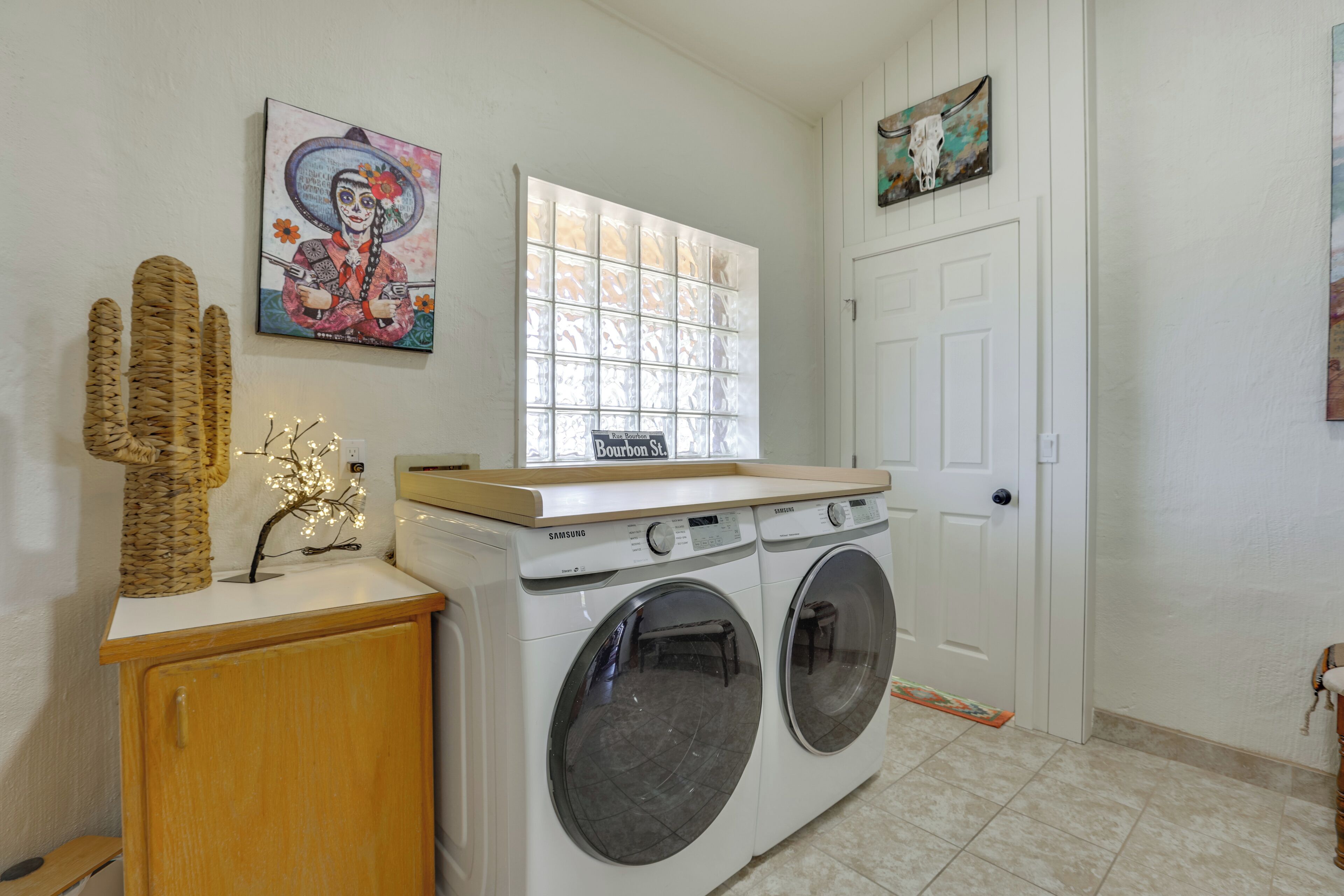 A laundry room with a washing machine, a drying rack, and decorative items including a woven basket and a small tree-like sculpture.