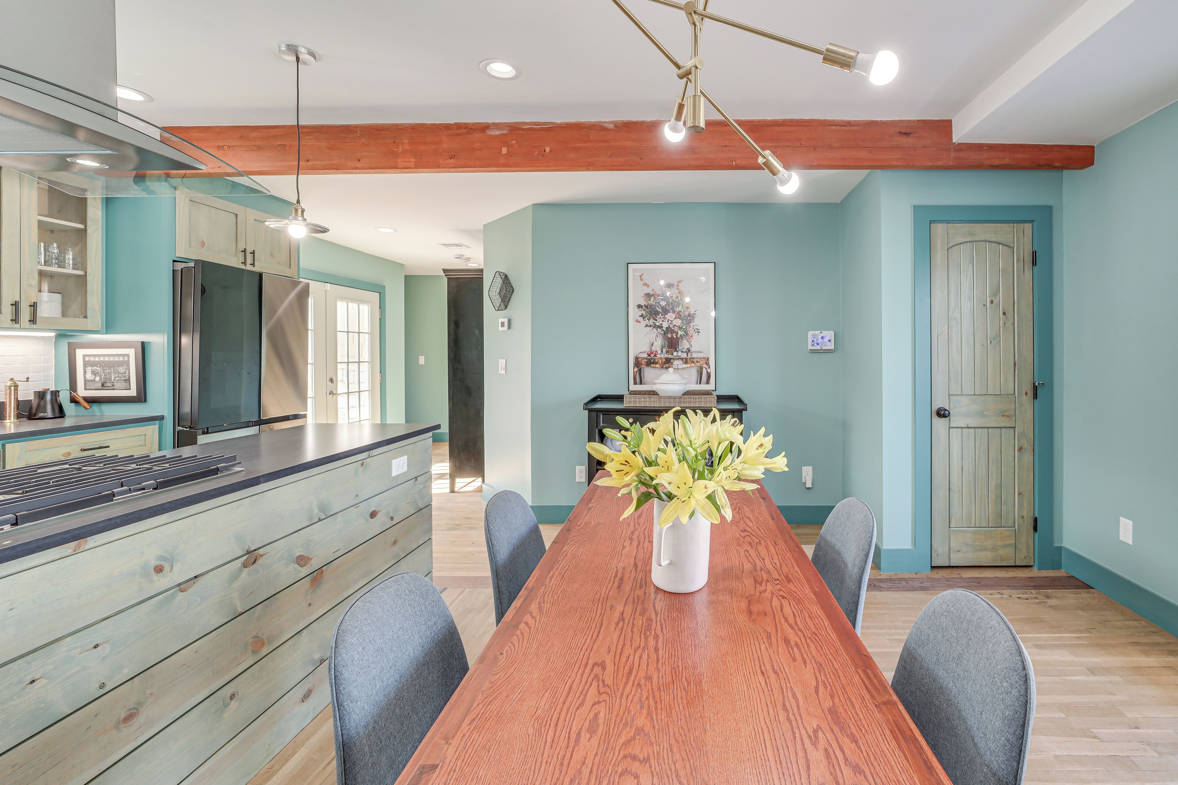 A modern kitchen with wooden cabinets, a stainless steel refrigerator, and a dining area with a wooden table and chairs.