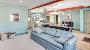 Un salon moderne avec un canapé bleu, un coin cuisine et des poutres en bois au plafond.