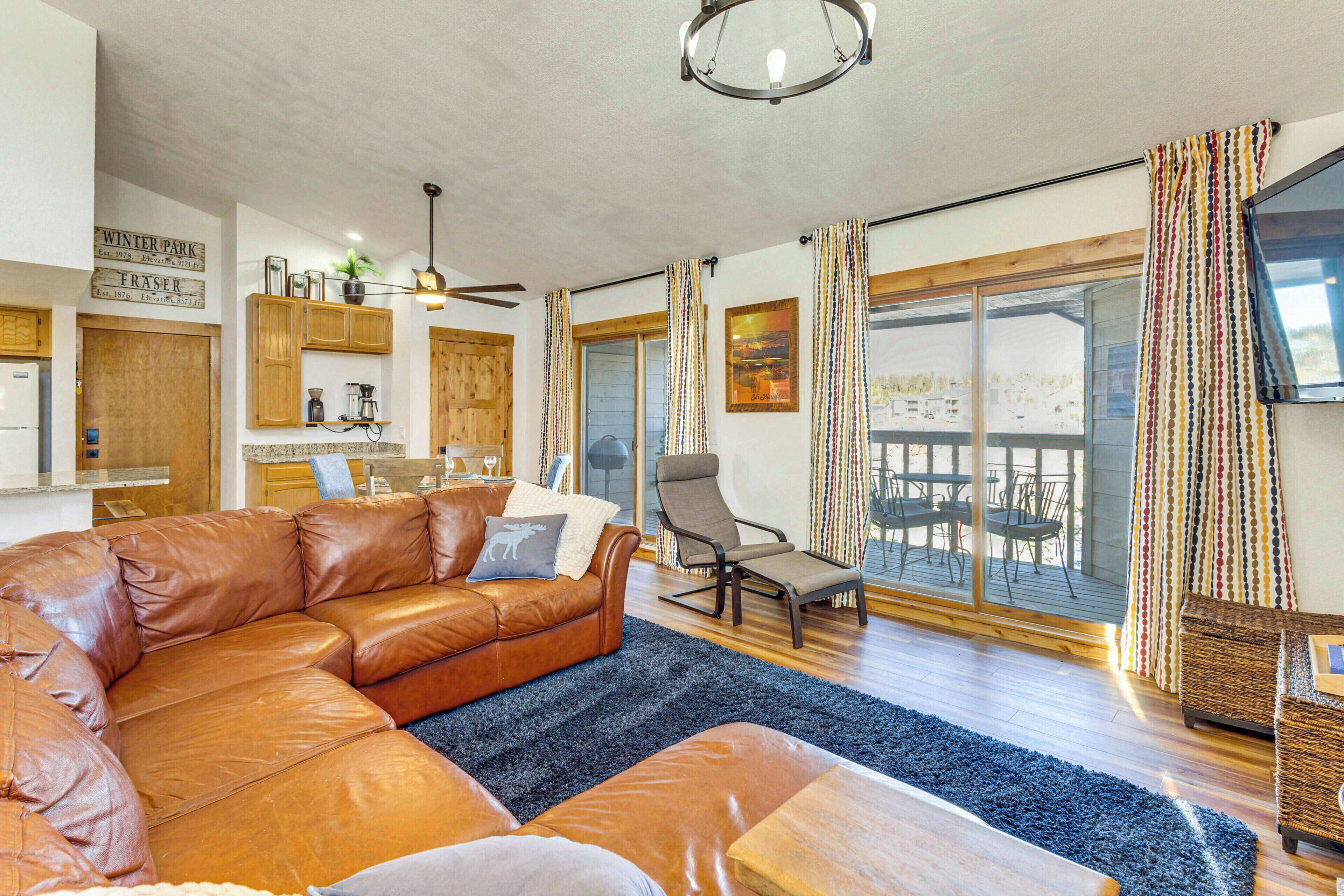 A spacious living area with a leather sofa, a dining table, and a kitchen in the background.