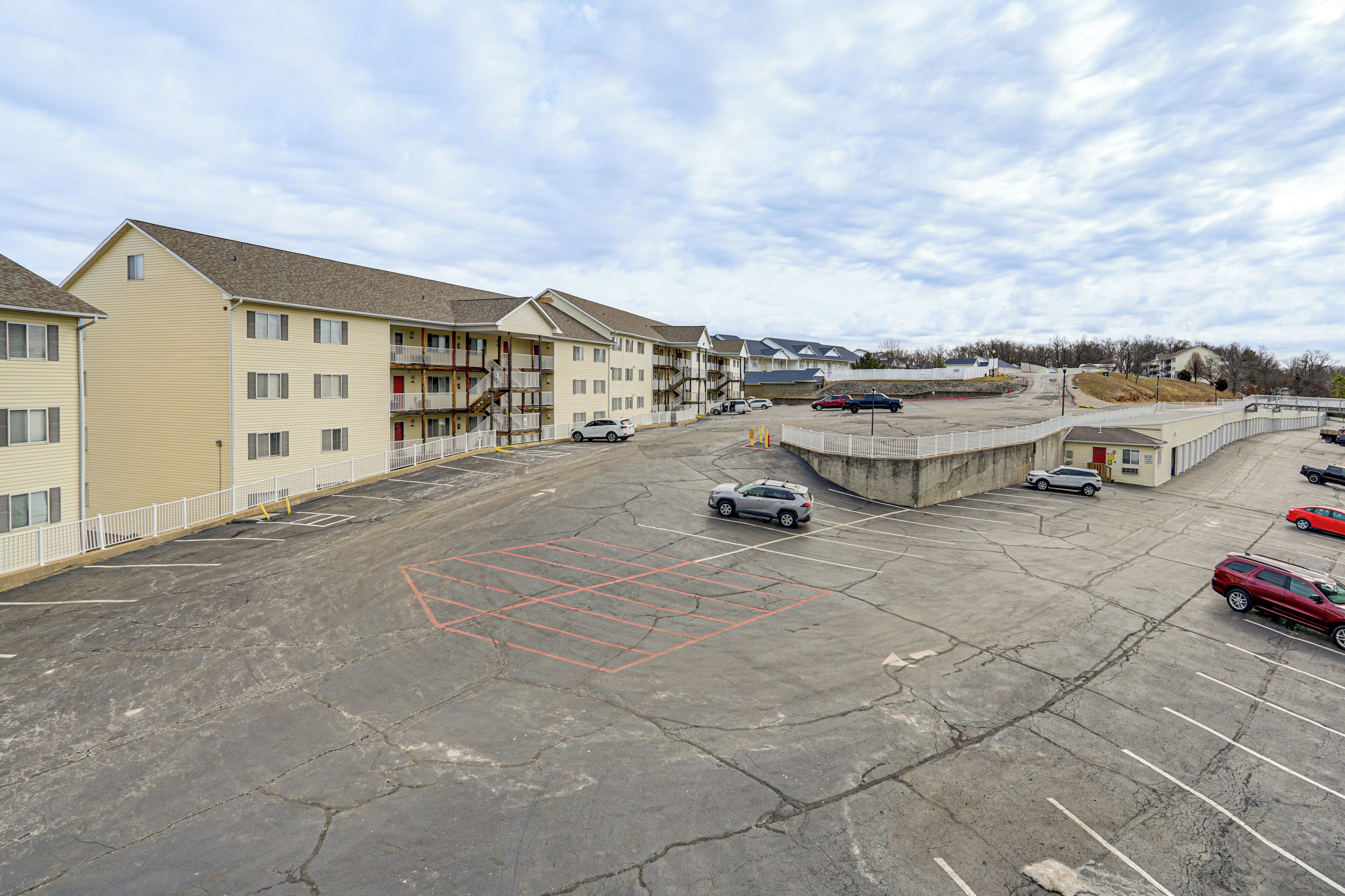Un parking rempli de voitures, un immeuble doté de balcons et un ciel dégagé.