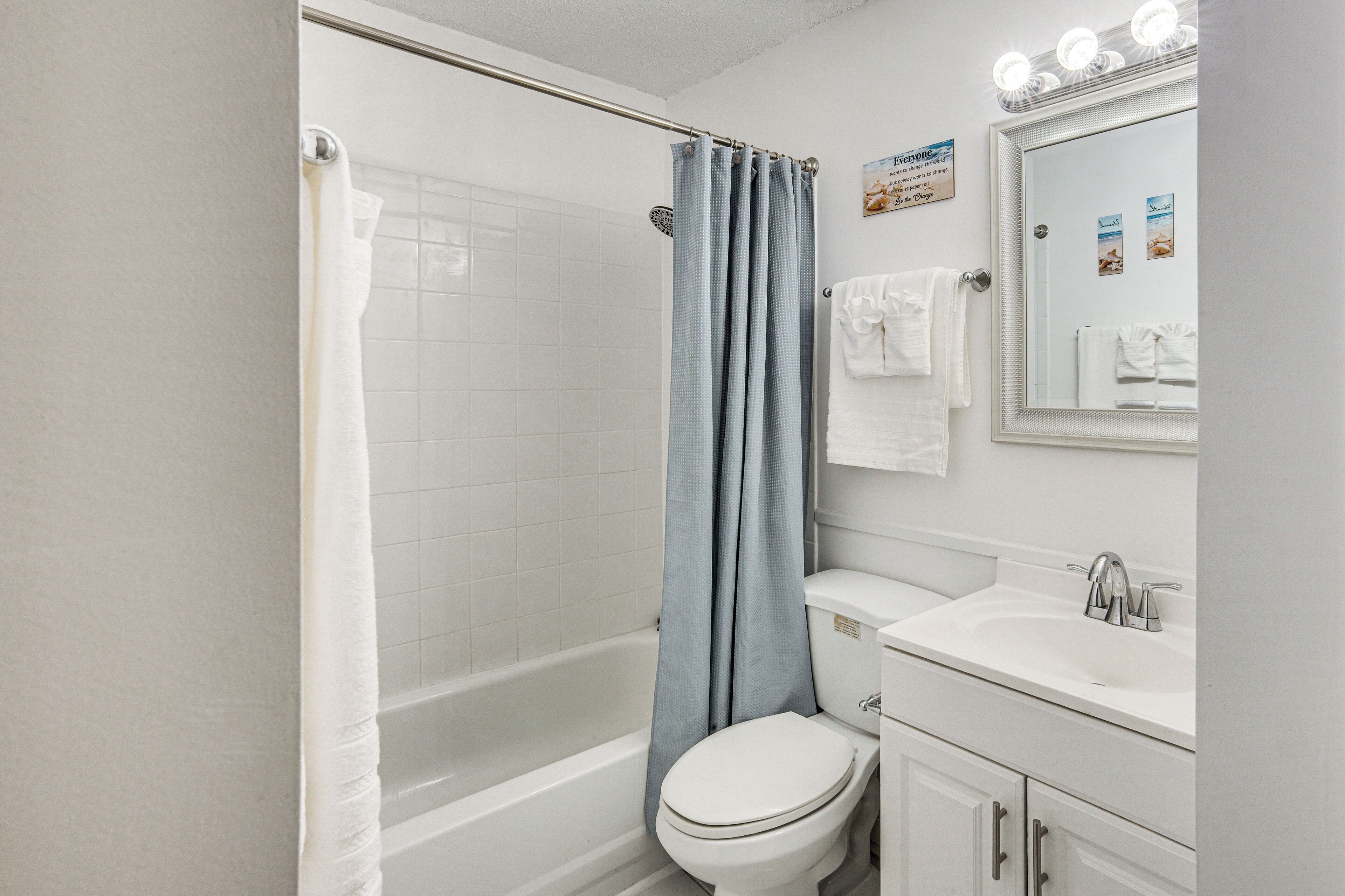 A bathroom with a shower, toilet, sink, and a mirror with lights.
