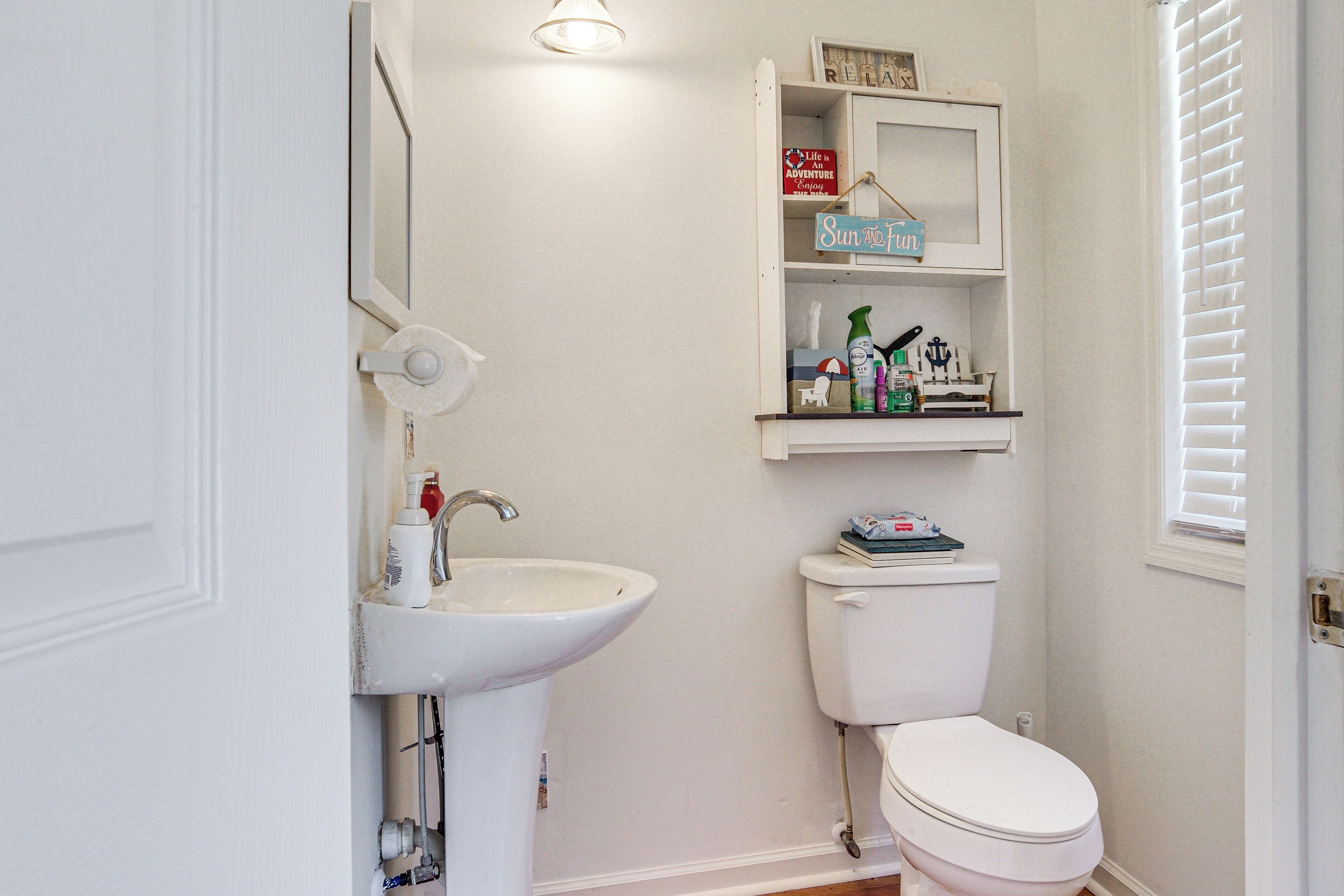 A bathroom with a white sink, toilet, and shelves with toiletries.
