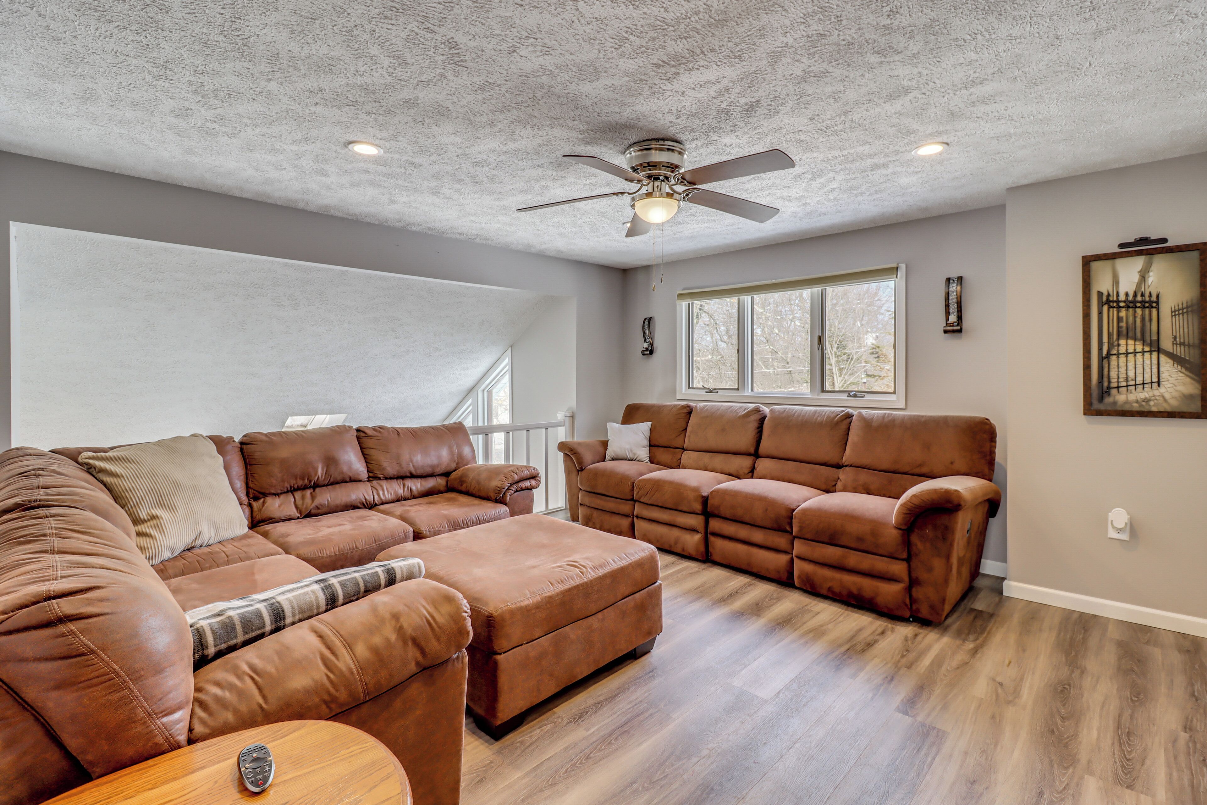 A spacious living room with a high ceiling, two brown leather sofas, a wooden coffee table, and a ceiling fan.