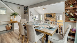 A dining area with a wooden table set for four, surrounded by grey upholstered chairs. A staircase is visible in the background leading to another level. - Contemporary House in Lakeside Community! Poconos (Albrightsville)