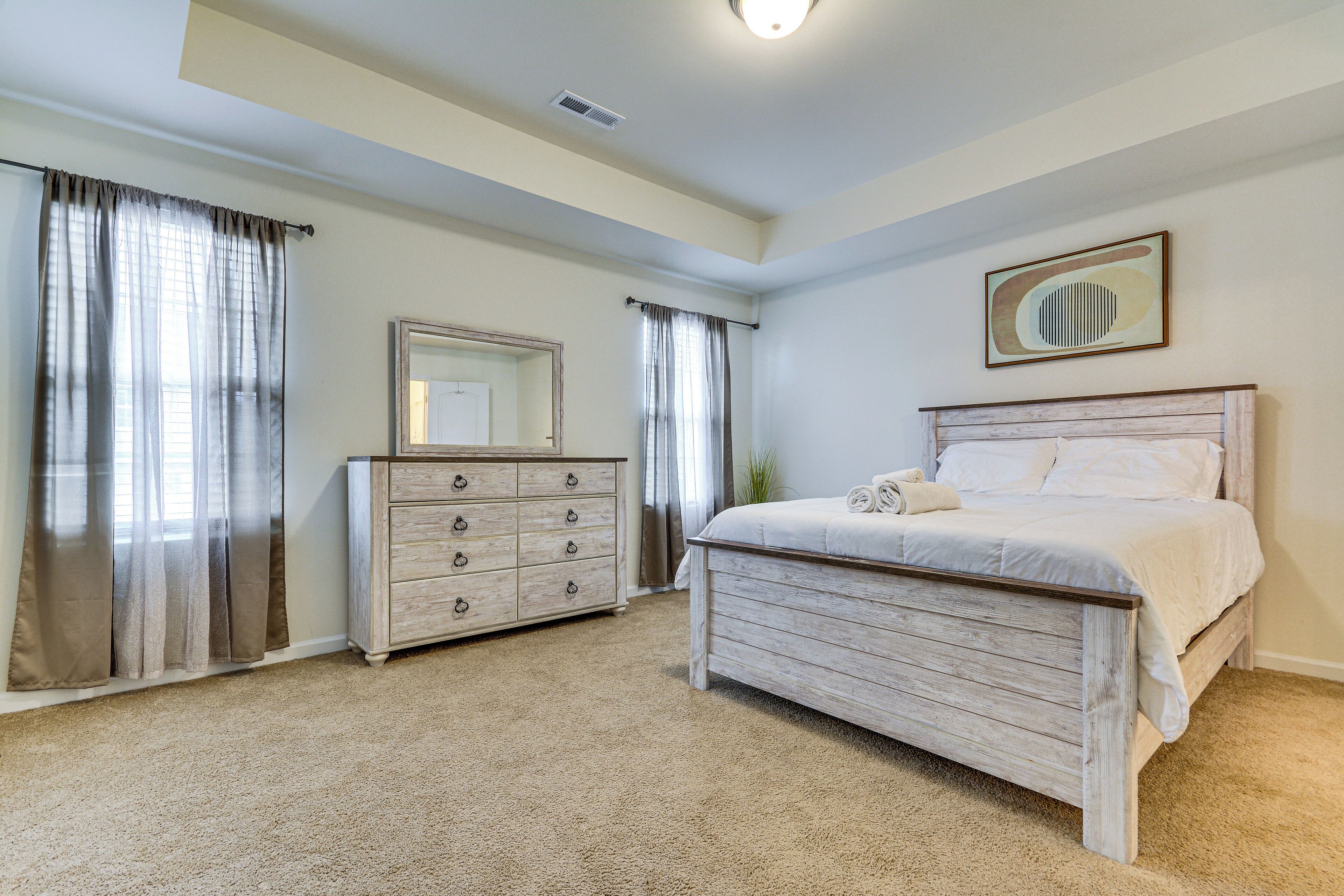 A bedroom with a bed, a dresser, a mirror, and curtains.