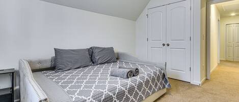 Een slaapkamer met een bed, twee kussens, een opgerolde handdoek, een nachtkastje en een kast.