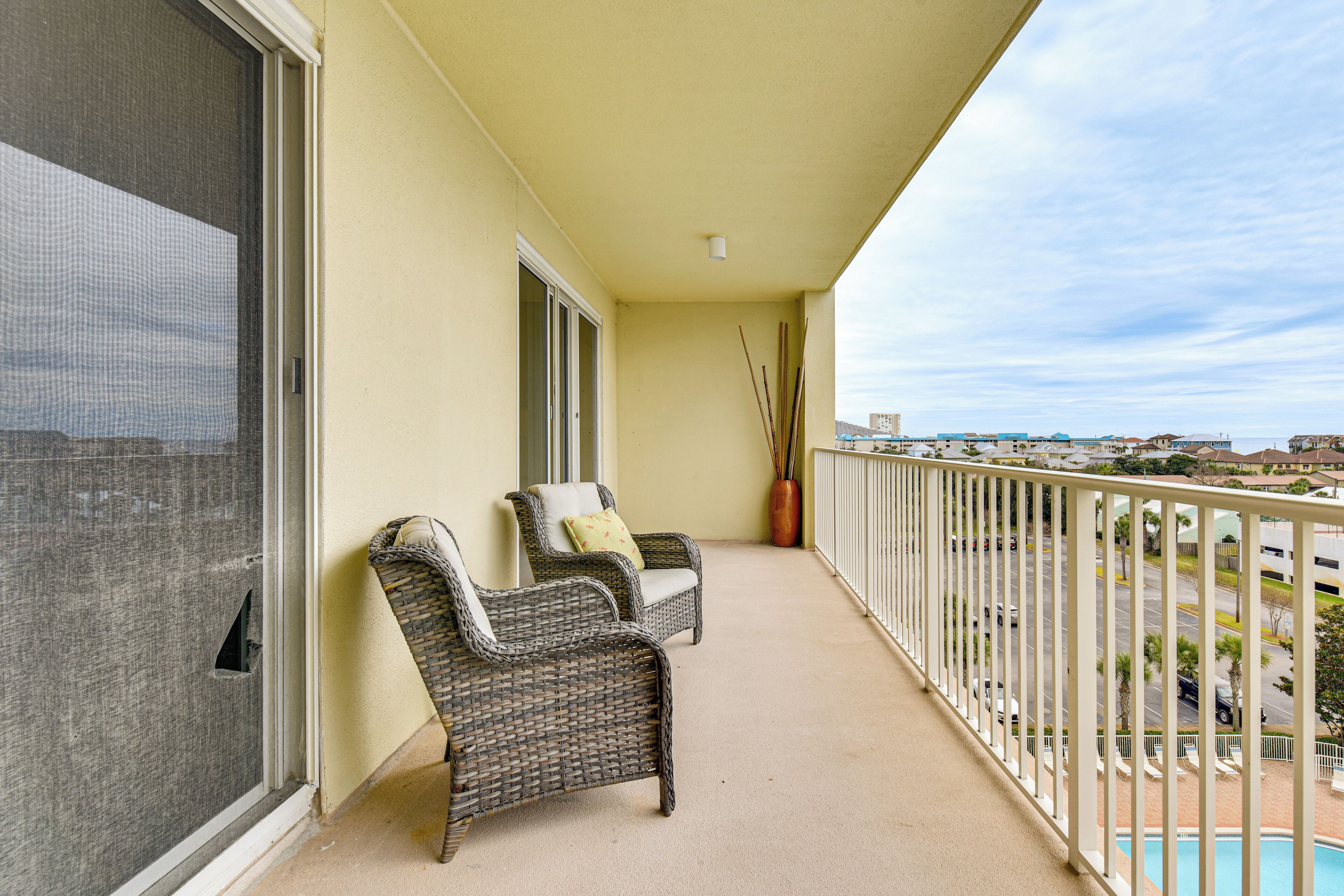A balcony with wicker chairs, a view of a parking lot, and a pool.