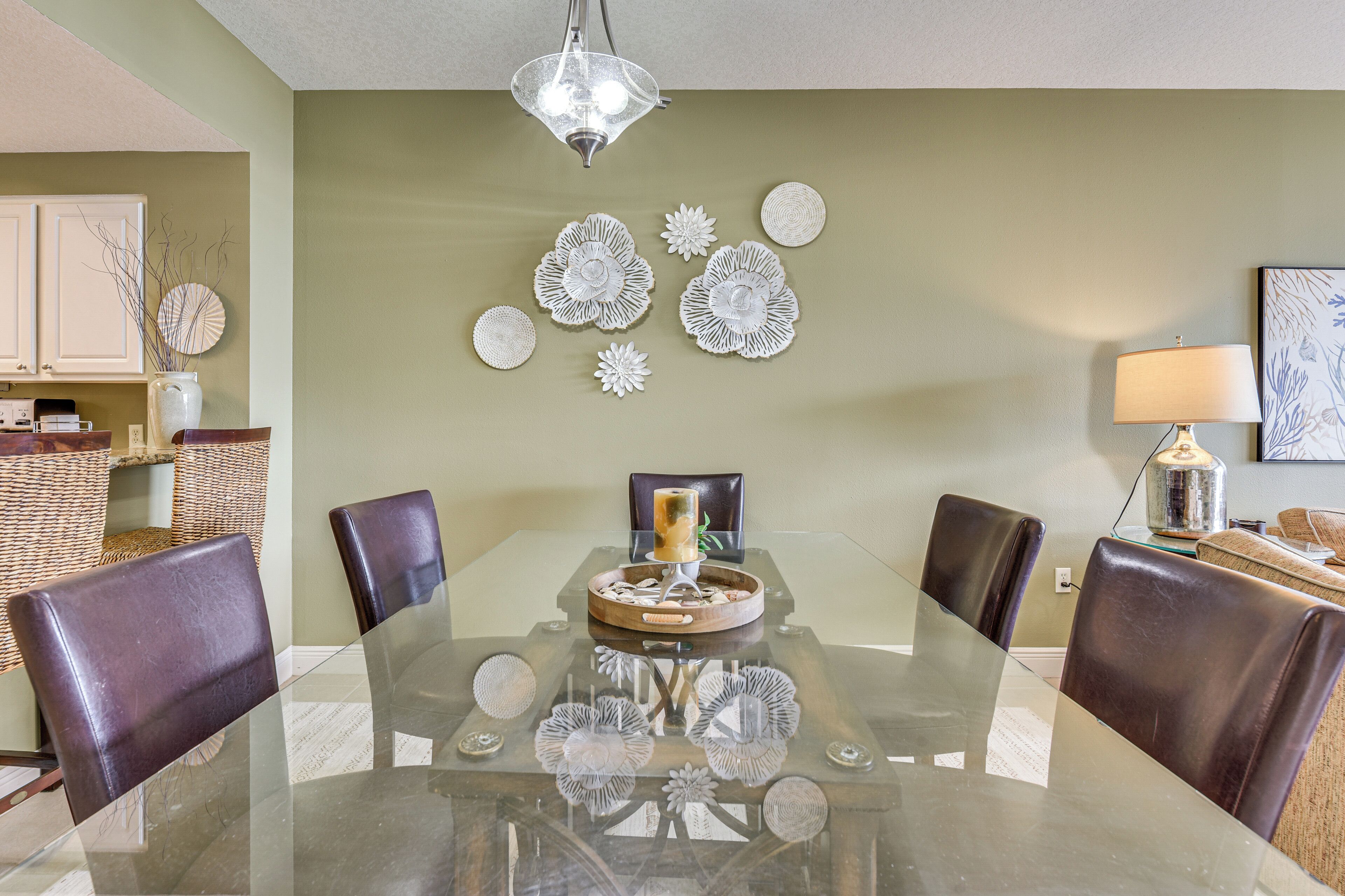 A dining area with a glass table, leather chairs, decorative wall art, and a hanging light fixture.