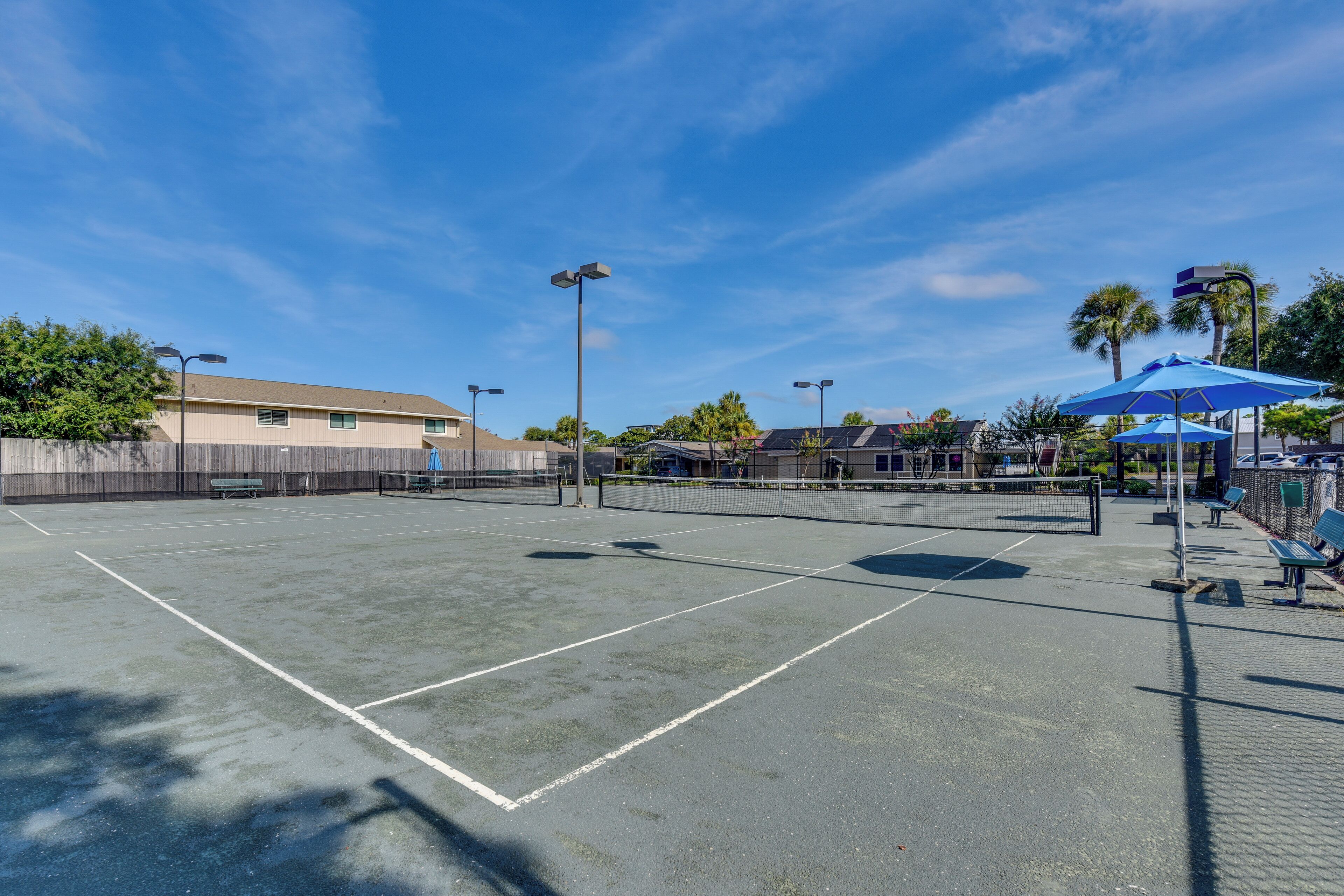 Una cancha de tenis exterior con red, bancos y sombrillas.