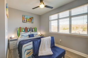 Un dormitorio con cama, ventilador de techo, ventana con persianas y un cuadro en la pared.