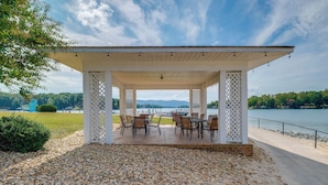 A covered outdoor seating area with tables and chairs, overlooking a body of water and mountains. - Surfboard-themed Huddleston Studio w/ Beach Access (Huddleston)