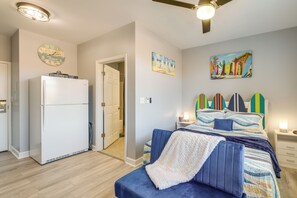 A bedroom with a bed, a white refrigerator, a ceiling fan, and a door leading to another room. - Surfboard-themed Huddleston Studio w/ Beach Access (Huddleston)