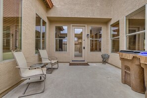 An outdoor patio area with a concrete floor, two white rocking chairs, a small table, and a trash bin. - 5 Mi to San Tan Mtn: San Tan Valley Group Getaway! (San Tan Valley)