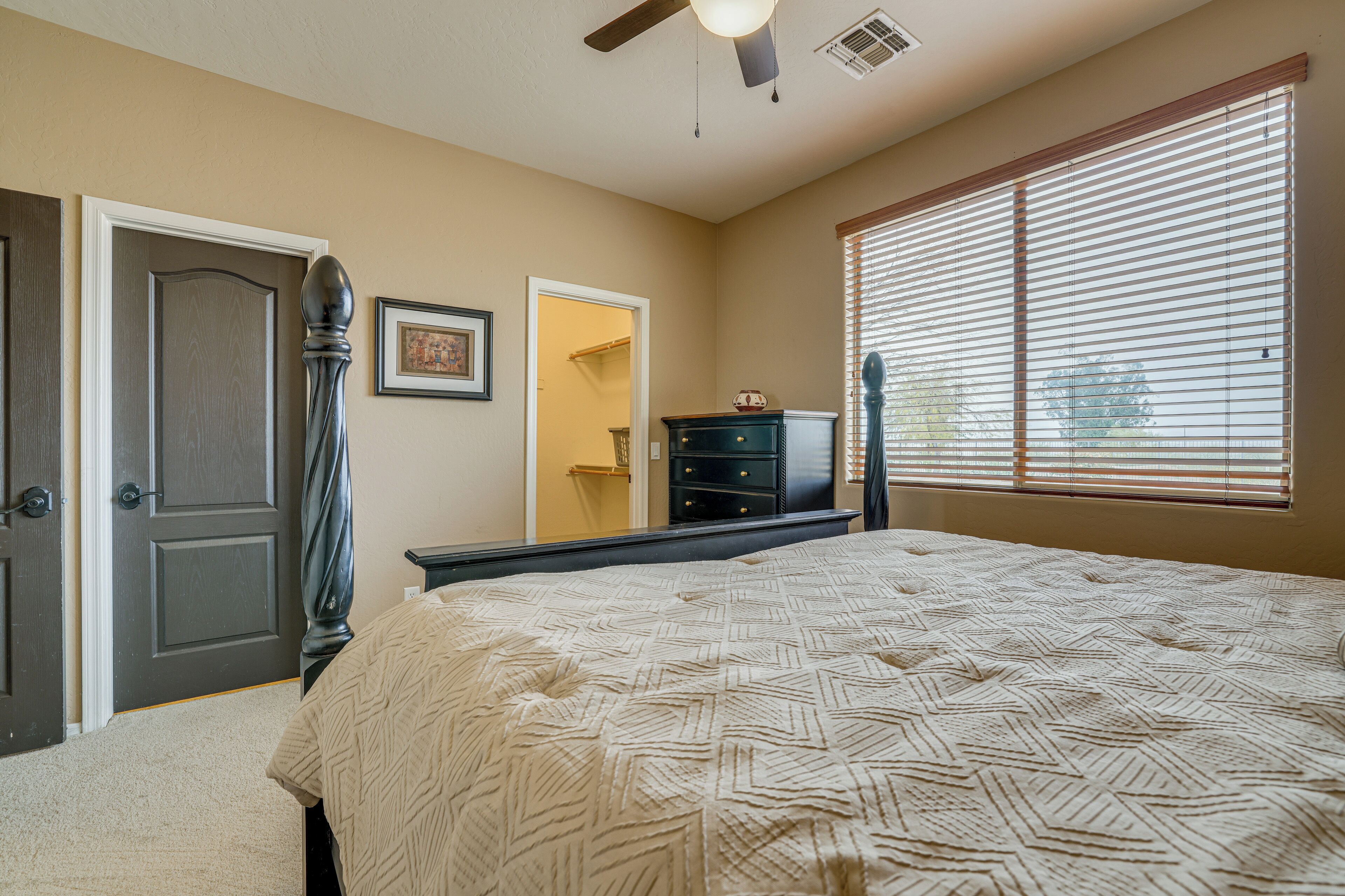 A bedroom with a large bed, a dresser, a door, and a window with blinds.