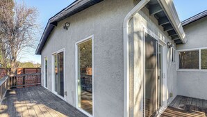 A covered patio with wooden decking, a white exterior wall, and sliding glass doors leading to a deck area.