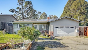A single-story house with a garage, a front yard with raised garden beds, and a large tree in the background.