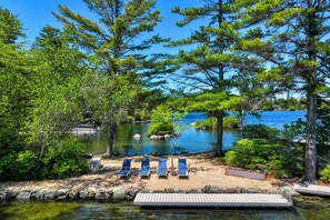 A lakeside view with a dock, lounge chairs, and a wooden bench. - Beach & Mtn Views! Lakefront Moultonborough Home (Moultonborough)